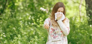 Young woman in grassy field with tissue over her mouth as if suffering from allergies