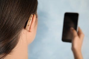 woman wearing hearing aid looking at phone