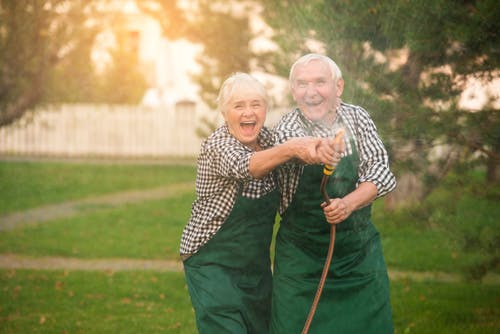 Older man and woman wearing aprons spraying a hose and laughing