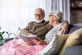 Smiling older couple sitting on couch reading a book together