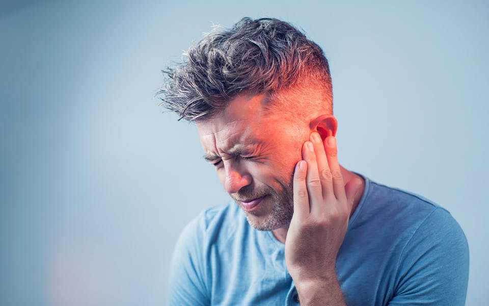 Male having ear pain touching his painful head isolated on gray background