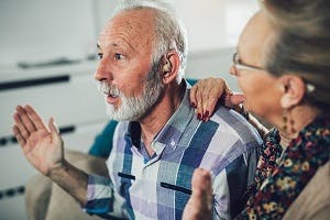 Older man wearing hearing aids looking surprised while his wife has her hand on his shoulder