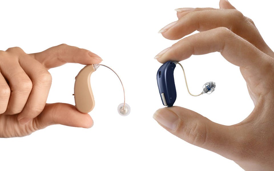 close up of a hearing amplifier and a hearing aid being held by separate hands